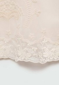 Delikatna koronkowa tkanina w kolorze kremowym z misternym haftem kwiatowym i falbaniastymi brzegami na przezroczystym tle siatki.