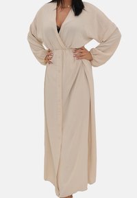 Beige wikkeljurk met lange mouwen, een v-hals en knopen aan de voorkant. Gemaakt van zachte, vloeiende stof met een elastische taille voor een gevormde pasvorm.