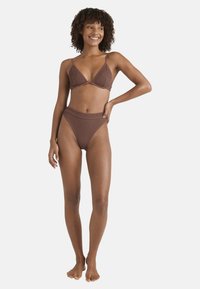 Bikini marrone a costine con top triangolare e parte inferiore a vita alta, dotato di spalline sottili e finitura testurizzata, indossato da un modello in piedi.