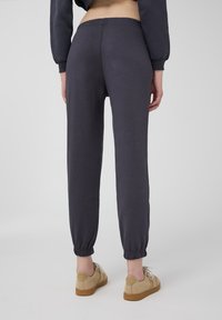 Ciemnoszare dresowe spodnie z elastycznym paskiem w talii i mankietami, wykonane z miękkiego materiału, w połączeniu z beżowymi sneakersami. Minimalistyczny design.