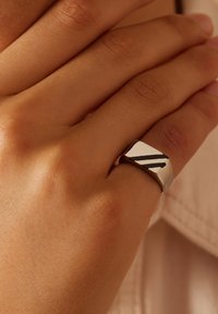 Zilveren ring met een geometrisch ontwerp en twee zwarte strepen, glanzende afwerking en een gladde, ronde band, gedragen op een hand.