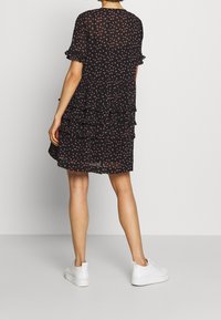 Czarna sukienka warstwowa z małymi różowymi wzorami kwiatowymi, krótkimi falbaniastymi rękawami i luźnym krojem, zestawiona z białymi trampkami.