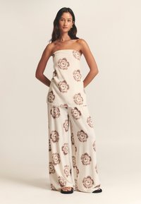 Dvisluoksnis komplektas iš lino, dekoruotas gėlių raštais, smėlio spalvos, su be petnešėlių viršumi ir plačiomis kelnėmis. Savybės: rudi gėlių akcentai ir laisvas kirpimas.