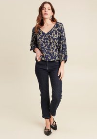 Bloemmotief blouse in marineblauw en olijf, met een v-hals en pofmouwen, gecombineerd met donkere spijkerbroeken en zwarte puntige flats.