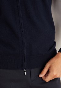 Marinblå zip-up tröja i lätt stickad material. Har en ribbad nederkant och muddar, samt en silverfärgad dragkedja vid kragen.