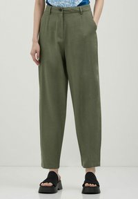 Pantalons en lin vert olive à coupe décontractée, dotés de deux poches latérales, d'une fermeture à bouton et d'une texture lisse. Associés à des sandales à talons blocs noires.