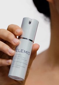 Weißer zylindrischer Serumflakon mit silbernem Akzent, beschriftet mit "ELEMI S DYNAMIC RESURFACING SUPER-C SERUM", gehalten von einer Hand.