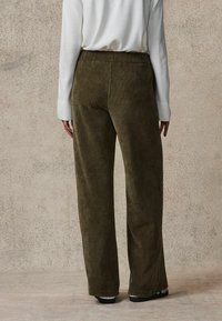 Szerokie spodnie z korduroy w oliwkowym kolorze, o miękkiej fakturze, elastycznym pasie i subtelnym pionowym prążkowanym wzorze.