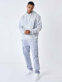 Felpa blu chiaro con un motivo sottile, abbinata a pantaloni cargo grigi chiari con tasche e una vestibilità comoda, completata da sneakers bianche.