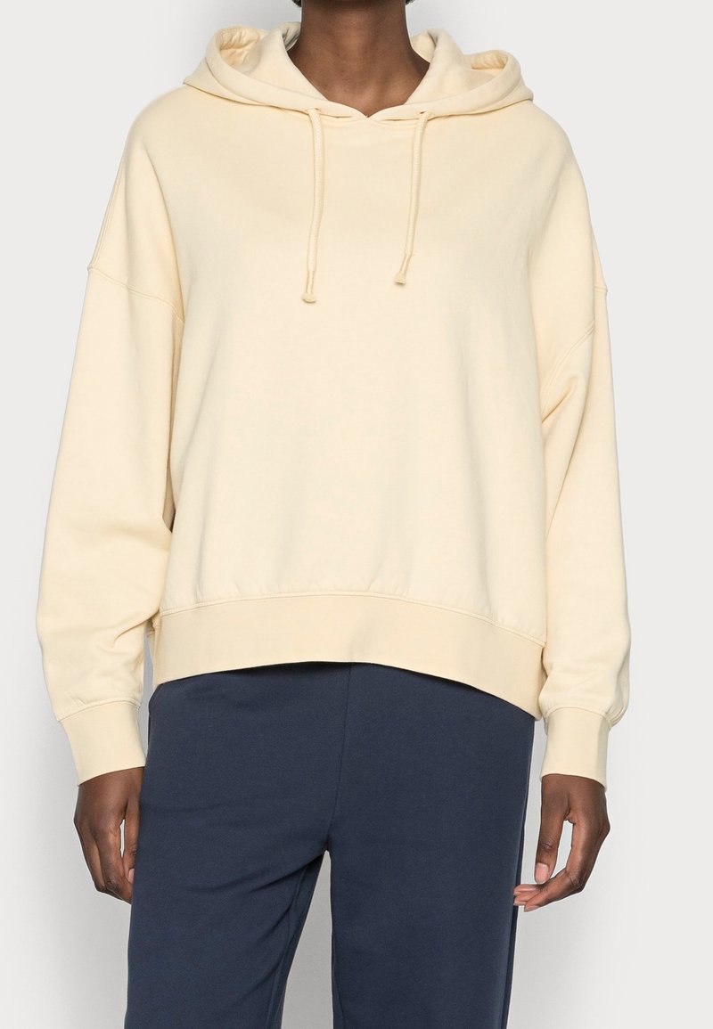 Krämfärgad huvtröja med dragsnören, oversized design, ribbad fåll och muddar, tillsammans med mörkblå byxor. Mjuk bomullsmaterial.