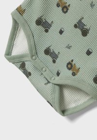 Combinaison en coton vert menthe avec des motifs de tracteurs. Présente une texture côtelée, des fermetures à pression et une doublure blanche contrastante.