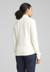 Haut à manches longues crème clair avec un col haut, texture lisse et design ajusté. Présente des coutures plates et une silhouette légèrement dessinée.