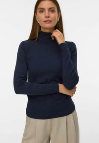 Tumši zilas krāsas turtlenecks džemperis ar garām piedurknēm, izgatavots no mīksta adījuma. Iezīmējas ar ribotiem elementiem apkaklē un rokā.