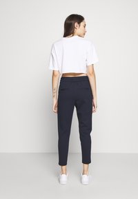 Kuttet hvit t-skjorte og mørk marineblå bukser med elastisk midje, slim fit, to baklommer, kombinert med hvite sneakers.
