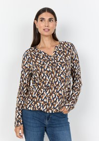 Langärmlige Bluse mit einem geometrischen Muster in Braun-, Weiß- und Blautönen, mit V-Ausschnitt und weichem Stoff. Kombiniert mit blauen Jeans.