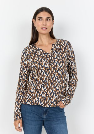 Langärmlige Bluse mit einem geometrischen Muster in Braun-, Weiß- und Blautönen, mit V-Ausschnitt und weichem Stoff. Kombiniert mit blauen Jeans.