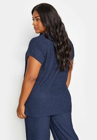 Marinblå topp med en strukturerad, krinklad design och korta ärmar, matchad med byxor i samma färg. Enkel, avslappnad passform med rundad halslinning.