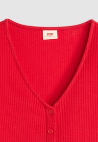 Crvena rebrasta pletena majica s dubokim V-izrezom, koja ima dva crvena gumba sprijeda i oznaku 'Levi's' unutar izreza.