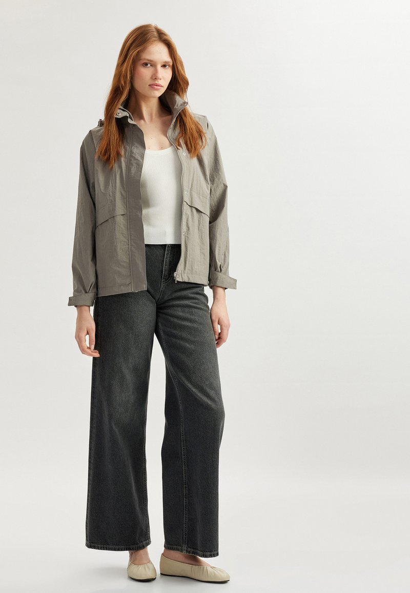 Grå lättviktsjacka med dragkedja, placerad över en vit ribbad topp, kombinerad med högmidjade mörk denimvida byxor.