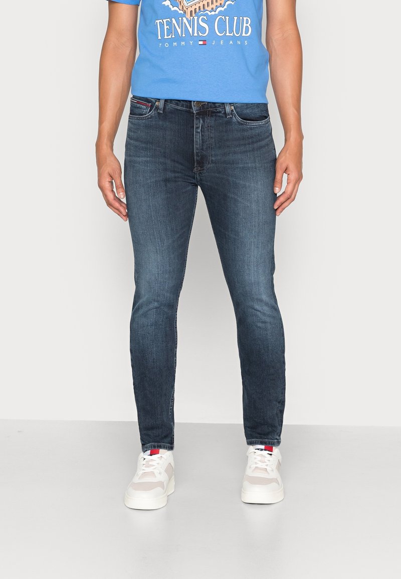 Mörkblå slim fit jeans i denim, med fem fickor och diskreta sömmar. Bärs tillsammans med en blå grafisk t-shirt och vita sneakers.