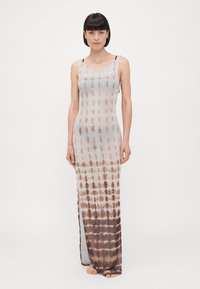 Long, sleeveless maxi dress in a light, sheer material with a brown and beige tie-dye pattern, featuring a flowy silhouette and side slits.