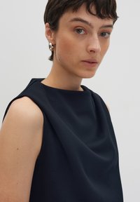 Navy sleeveless top with a draped design and textured fabric; features a wide neckline and subtle stitching along the shoulder seams.