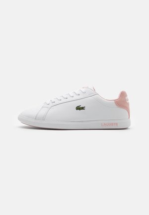 Scarpa da ginnastica bianca low-top con tallone e fodera interna rosa, logo coccodrillo verde sul lato, marchio "Lacoste" sulla suola e sulla linguetta del tallone.