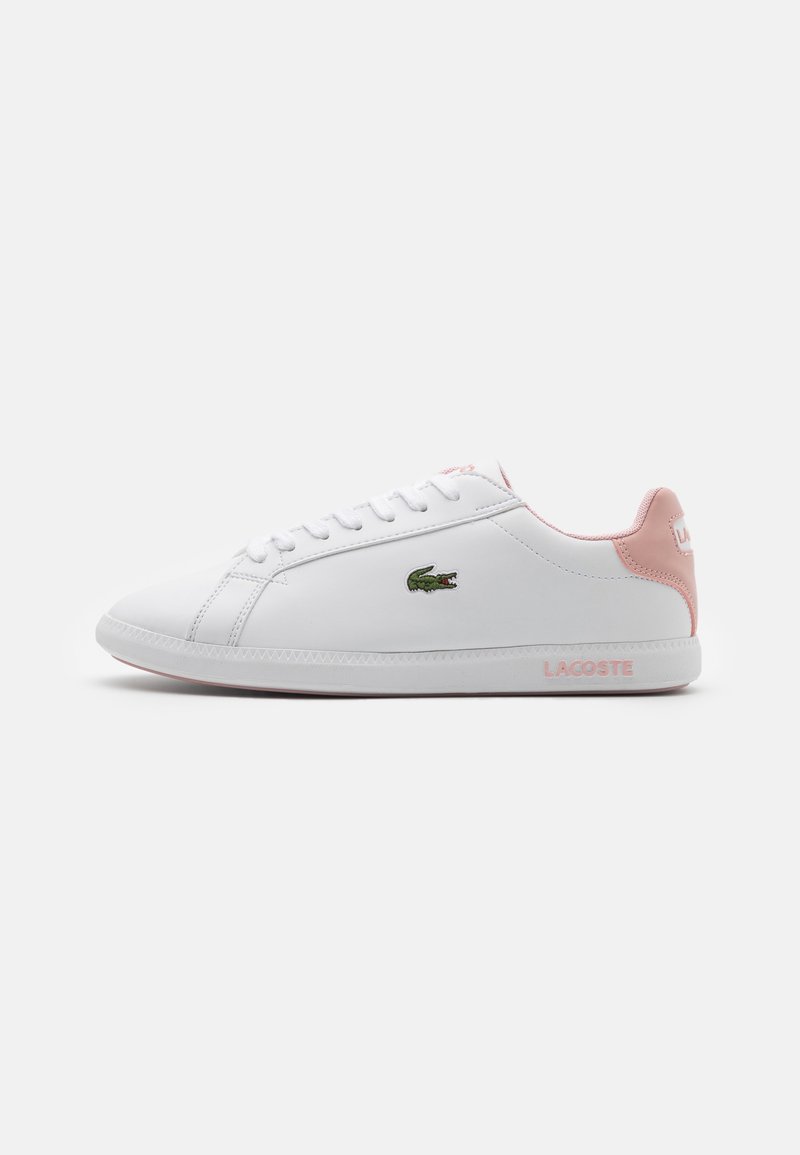 Baskets basses blanches avec talon et doublure intérieure roses, logo crocodile vert sur le côté, marque "Lacoste" sur la semelle et sur la languette du talon.