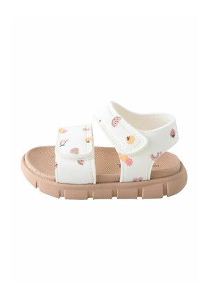 White toddler sandal with Velcro straps, floral and fruit patterns, and a light brown textured sole.