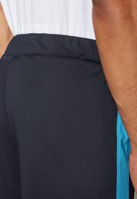 Shorts de sport noirs avec une bande latérale bleue, en matière lisse et extensible, dotés d'une taille élastique.