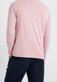 Camicia a maniche lunghe in morbido tessuto rosa, con scollatura rotonda e vestibilità rilassata, con cuciture decorative lungo le spalle e l'orlo.