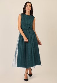 Tüllkleid in Türkis mit strukturiertem Spitzenoberteil und gewellten Abschlüssen, sowie einem gepunkteten Tüllrock. Es hat eine taillierte Passform und einen knöchellangen Stoff.
