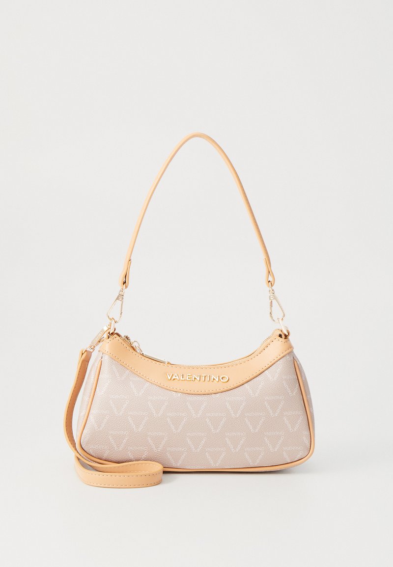 Beige handbag with tan leather accents, featuring a curved design, logo on the front, and a detachable shoulder strap. Subtle pattern throughout.
