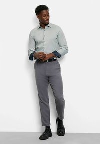 Hellgrünes Hemd mit Knöpfen und gemusterten Manschetten, kombiniert mit grauer Hose und schwarzen Schuhen. Einfaches Design, taillierte Form, glatte Textur.