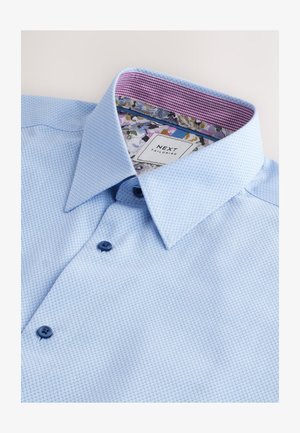 Hellblaues Hemd mit Knöpfen und strukturiertem Muster, mit einem lila Blumenmuster im inneren Kragen und dunkelblauen Knöpfen.