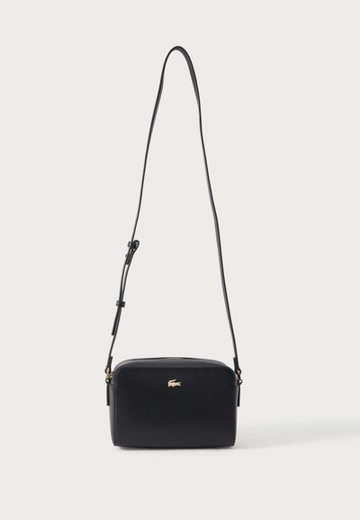Sac bandoulière rectangulaire noir avec bandoulière fine réglable et petit logo crocodile doré au centre avant.