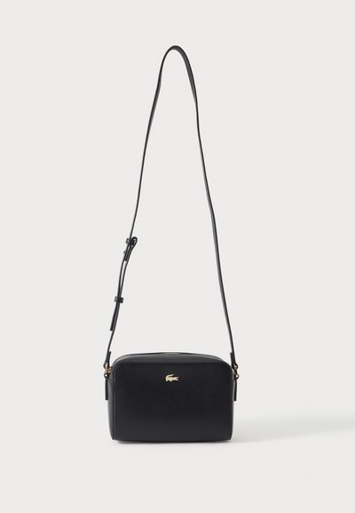 Sac bandoulière rectangulaire noir avec bandoulière fine réglable et petit logo crocodile doré au centre avant.