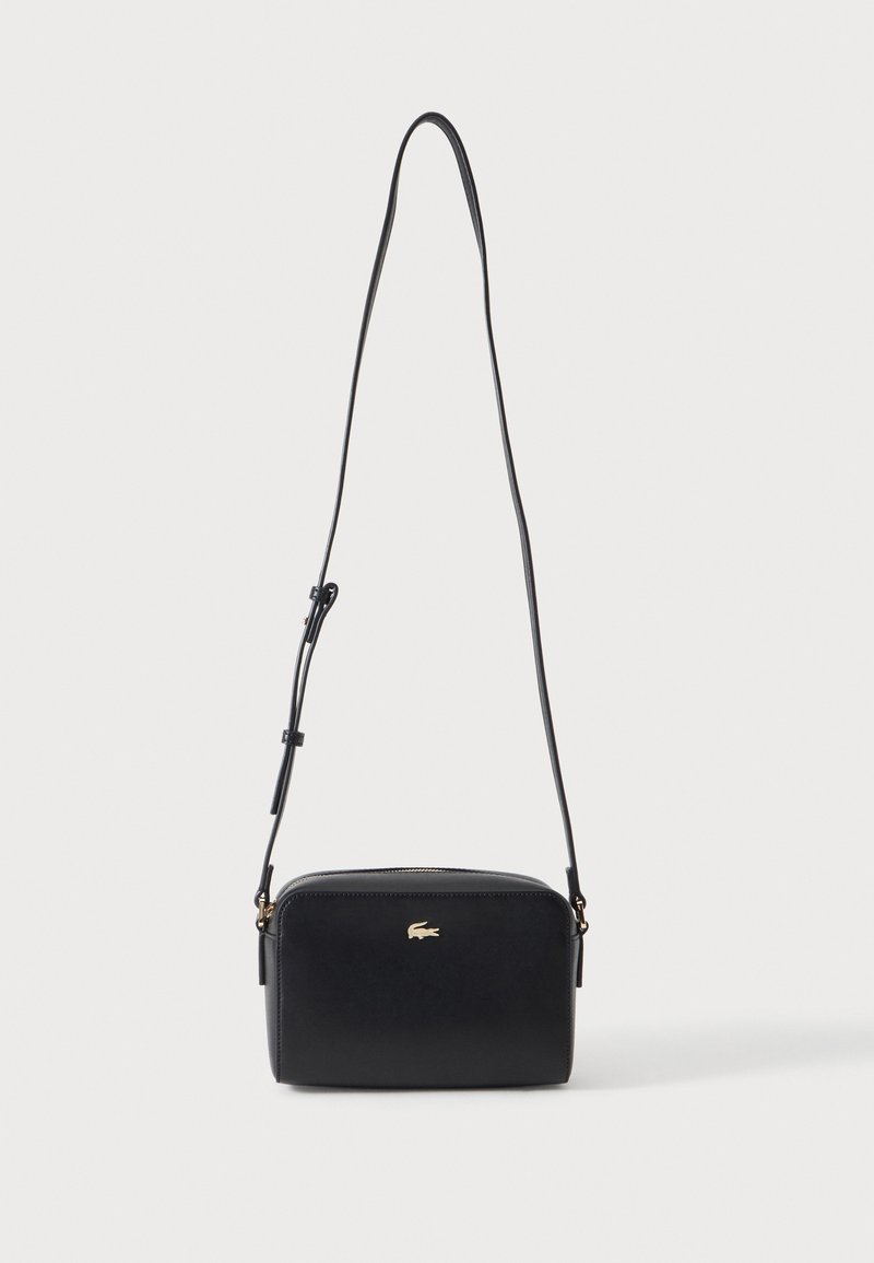 Sac bandoulière rectangulaire noir avec bandoulière fine réglable et petit logo crocodile doré au centre avant.