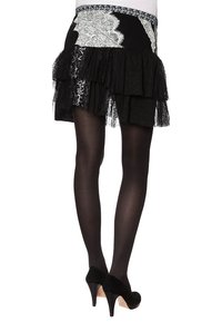 Schwarze schichtige Rock mit Spitze und strukturierten Akzenten, der einen fransigen Saum besitzt. Getragen mit blickdichten schwarzen Strumpfhosen und schwarzen spitzen Absätzen.