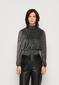 Top noir à manches longues avec un scintillement métallique, col haut et taille froncée ; associé à un pantalon en cuir noir, créant une silhouette structurée.