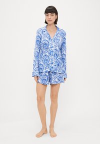 Blue and white patterned pajama set featuring long-sleeve shirt and shorts, made of lightweight fabric with a smooth texture and contrasting piping.