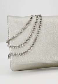 Borsa a tracolla sintetica argento con finitura testurizzata, caratterizzata da tre catene e una forma rettangolare elegante.