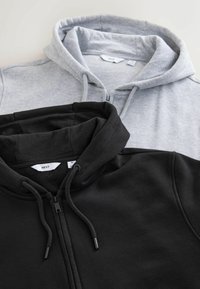 Dos sudaderas planas: una de color gris con cremallera y capucha ajustable en la parte superior y una de color negro con cremallera y capucha ajustable en la parte inferior. Ambas están fabricadas con un tejido suave.