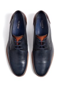 Laivastonsiniset nahkakengät, joissa on läpileikattu kuvio, ruskeat yksityiskohdat kannassa ja kontrastivärinen sininen sisäosa. Varustettu nauhoilla ja pyöreällä kärjellä.