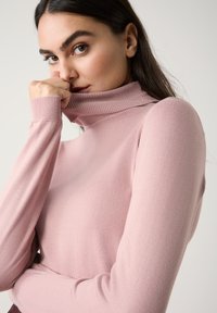 Rosa Rollkragenpullover aus weichem Stoff, mit langen Ärmeln und geripptem Kragen. Taillierter Schnitt mit glattem Material.