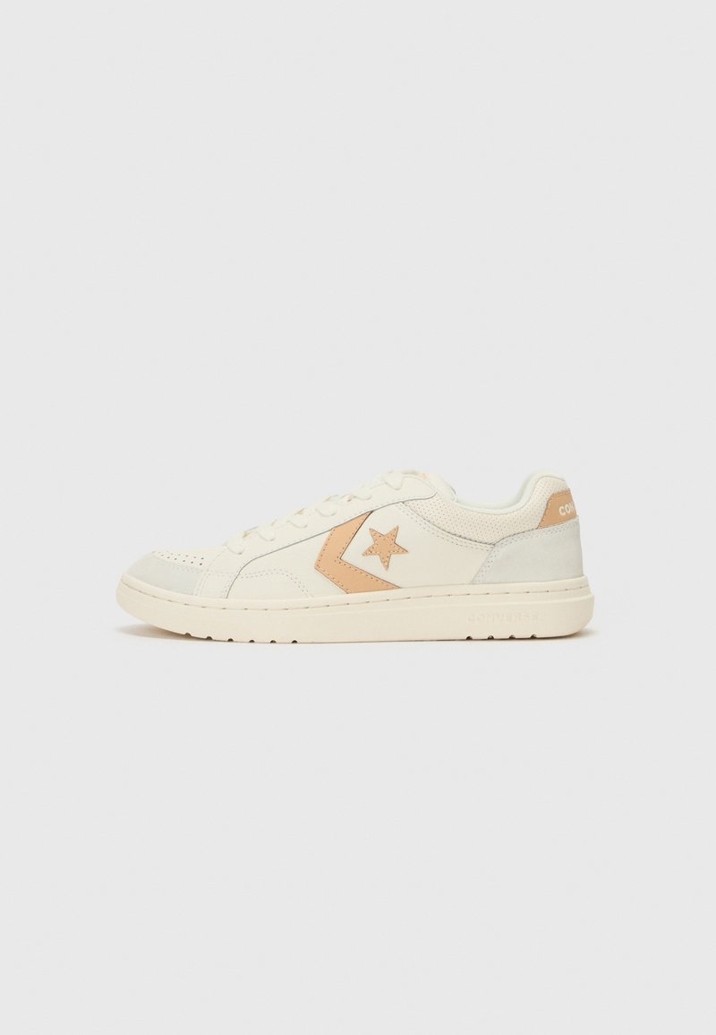 White sneakers with a beige star logo, leather and suede material, round toe, lace-up design, and a textured rubber sole.