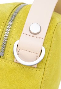 Geel suède tasje met een lichte leren band en zilveren beslag. Voorzien van een rits en een cirkelvormige bevestigingsring. Soepele textuur en levendige kleur.