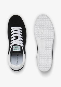 Baskets en daim noir avec lacets blancs et semelle extérieure en caoutchouc. Présentent un logo vert et blanc sur la languette et une semelle texturée pour une meilleure adhérence.