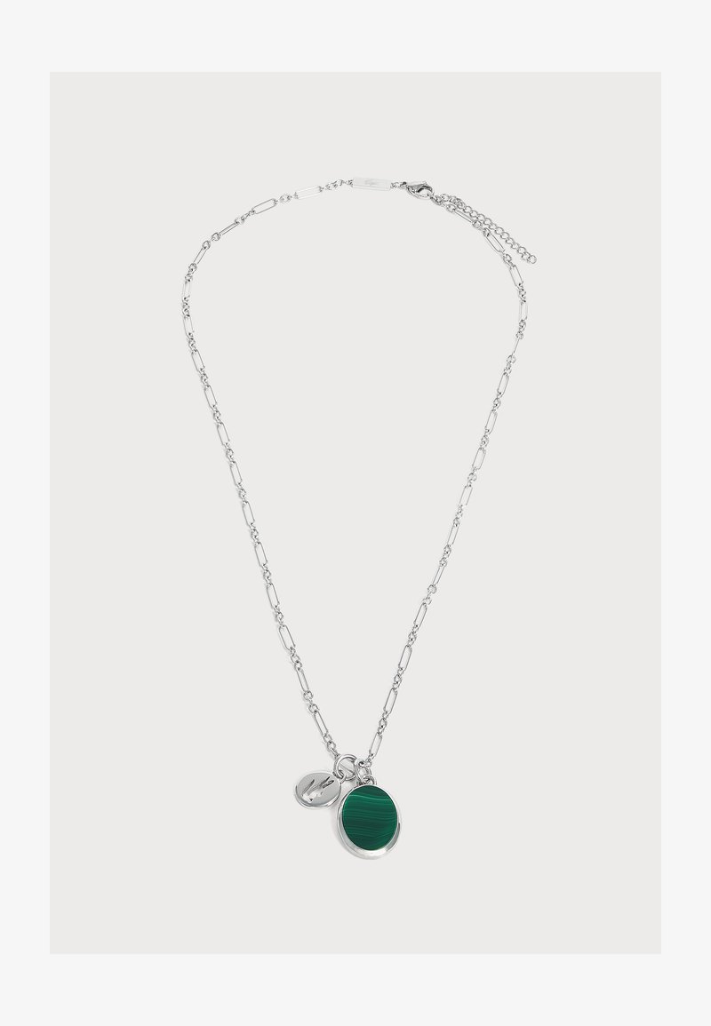 Collier chaîne en argent avec des maillons allongés, avec un pendentif rond en pierre verte et un petit charm en forme d’étiquette en argent.