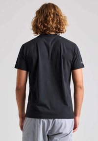 T-shirt nera a maniche corte realizzata in un tessuto morbido, con colletto rotondo e un design semplice, con un logo visibile sulla manica sinistra.